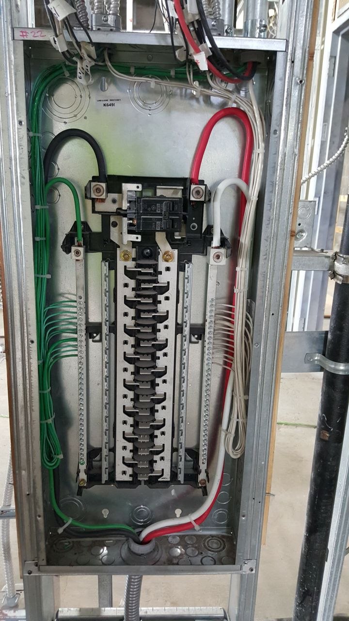 Open breaker panel during rough-in with neatly routed color-coded conductors landed on the bus and breakers